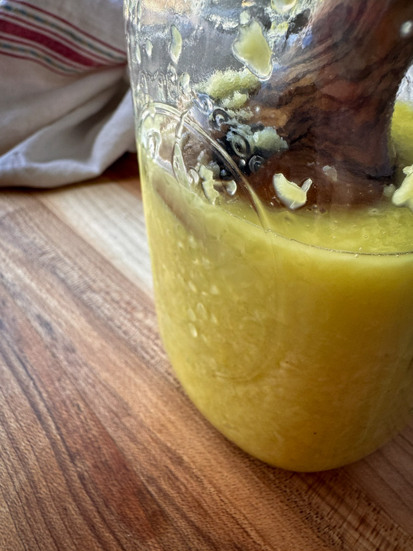 fermented ginger in a jar with a wooded kraut pounder
