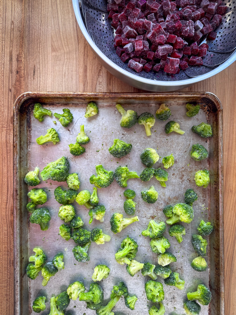 half sheet with small frozen broccoli florets ready to be baked and a steaming basket full of frozen beets